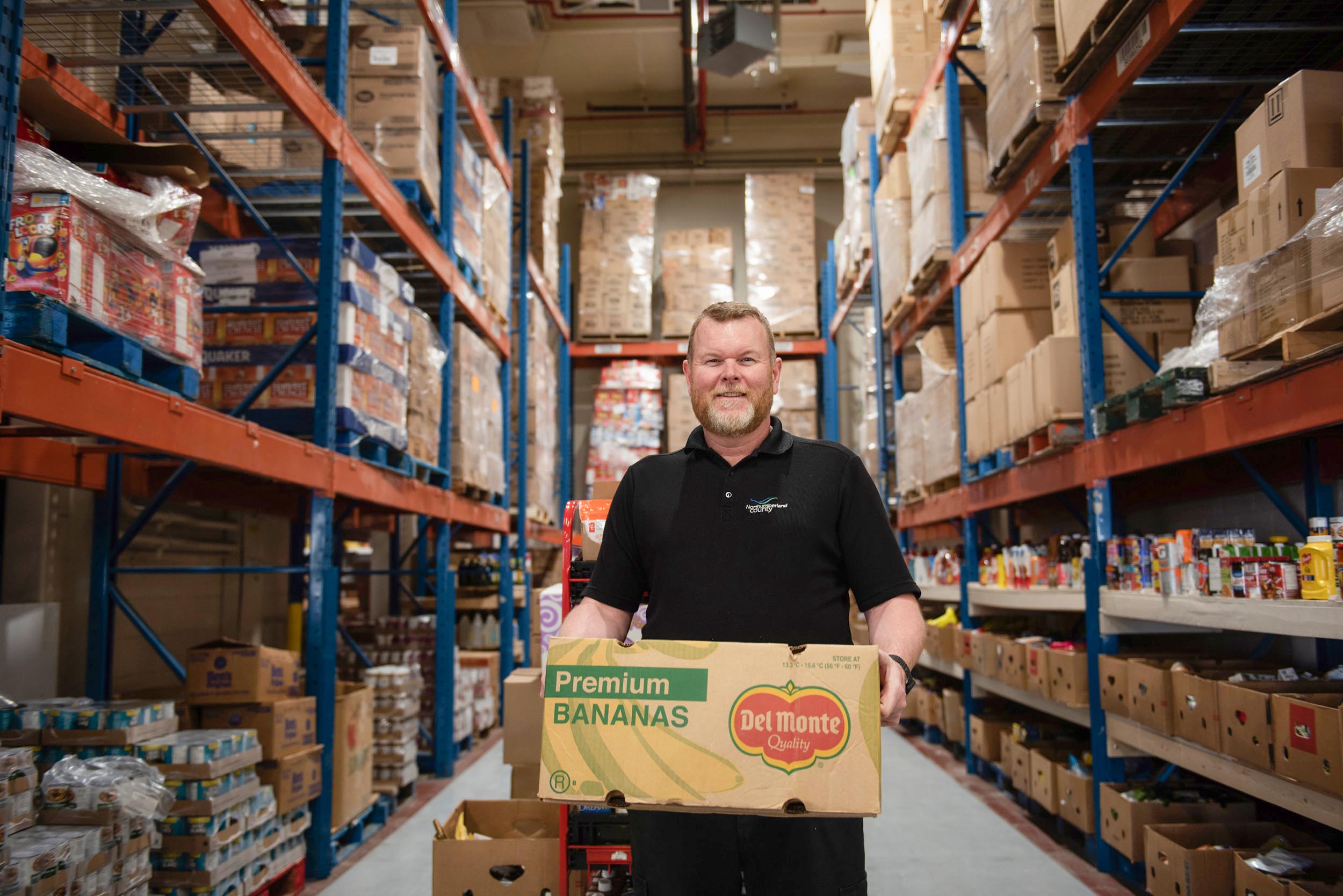 County staff member holding a box in the Food 4 All Warehouse.